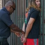 Police officer handcuffing a suspect during an arrest against an urban backdrop.