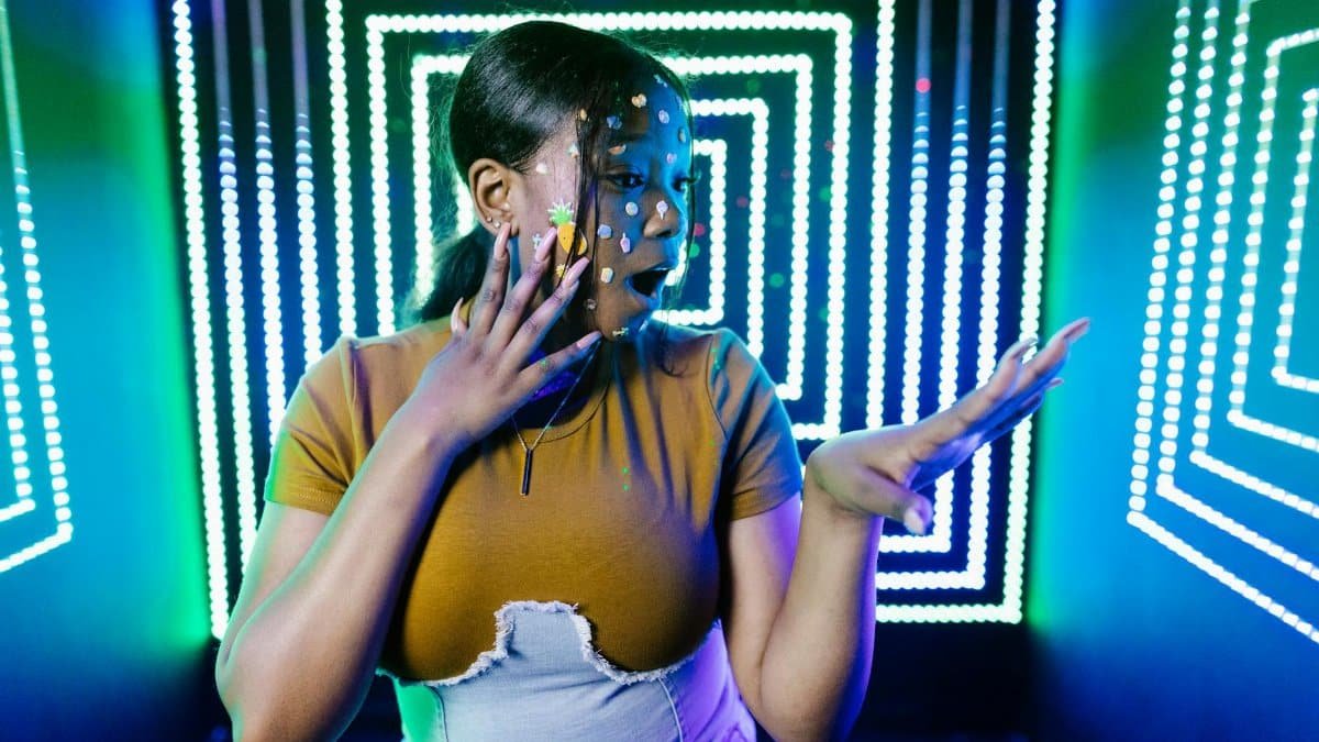 Surprised woman with facial decorations in a vibrant LED-lit room, expressing shock.