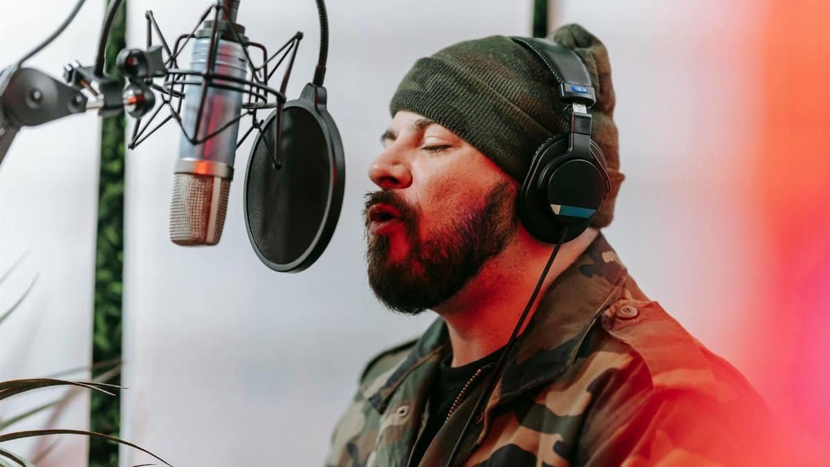 Bearded man in camouflage jacket singing into a microphone in a studio setting.
