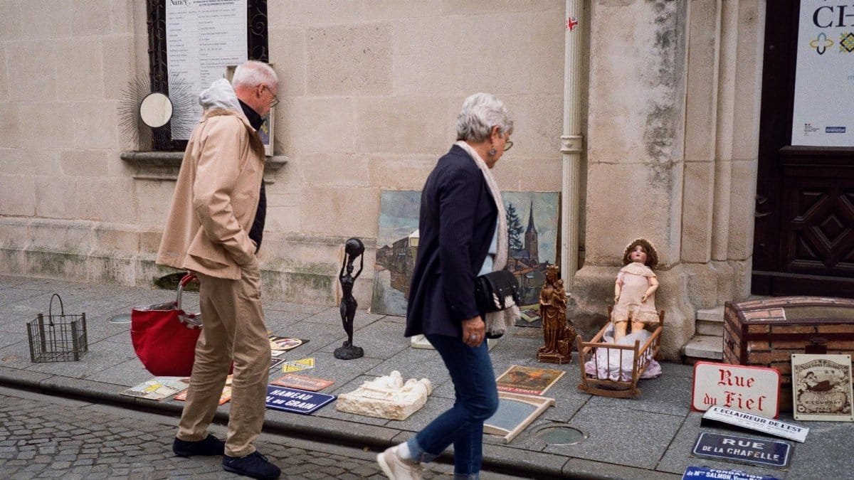 An elderly couple browses a vintage street market in Nancy, France. Historic charm and curiosity come alive.
