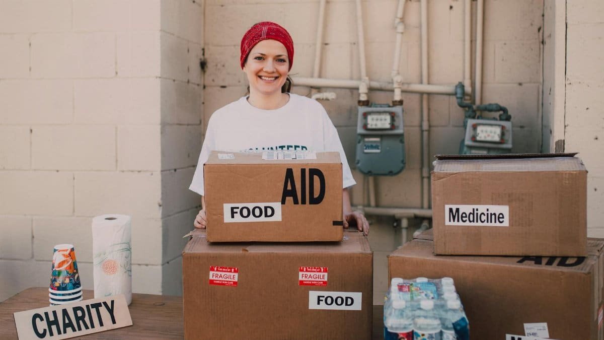 Woman volunteer distributing aid packages with food and medicine for charity outdoors.