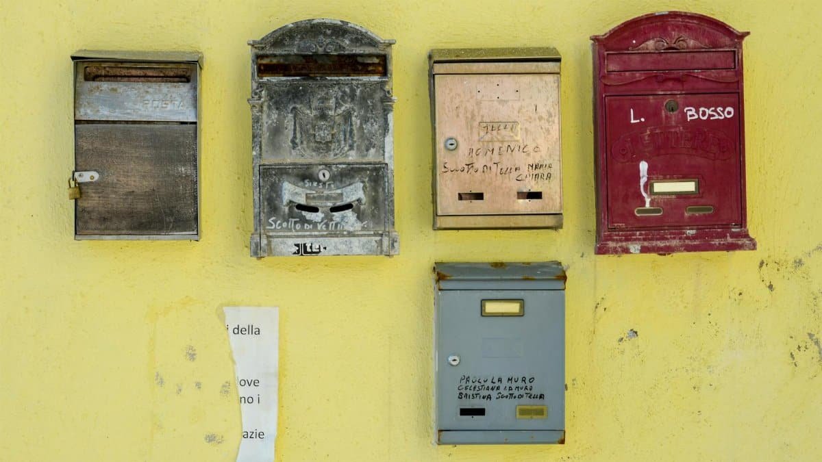 Five old mailboxes mounted on a distressed yellow wall, showcasing vintage charm.
