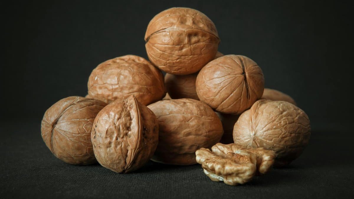 A detailed photograph of whole walnuts in shell, showcasing texture against a dark background.