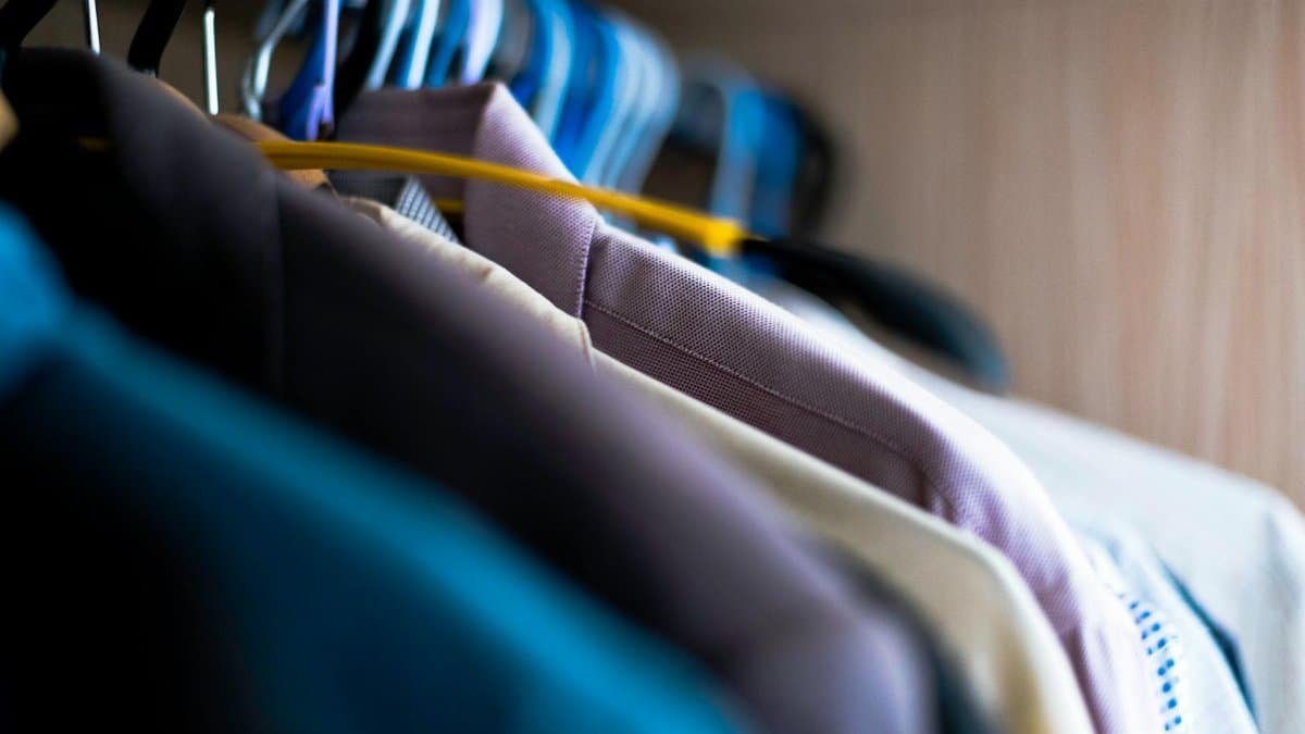 Close-up of various shirts hanging on colorful hangers inside a wardrobe.