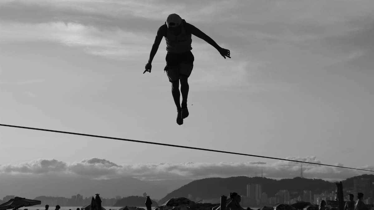 A silhouette of a man skillfully balancing on a tightrope at the beach during sunset.