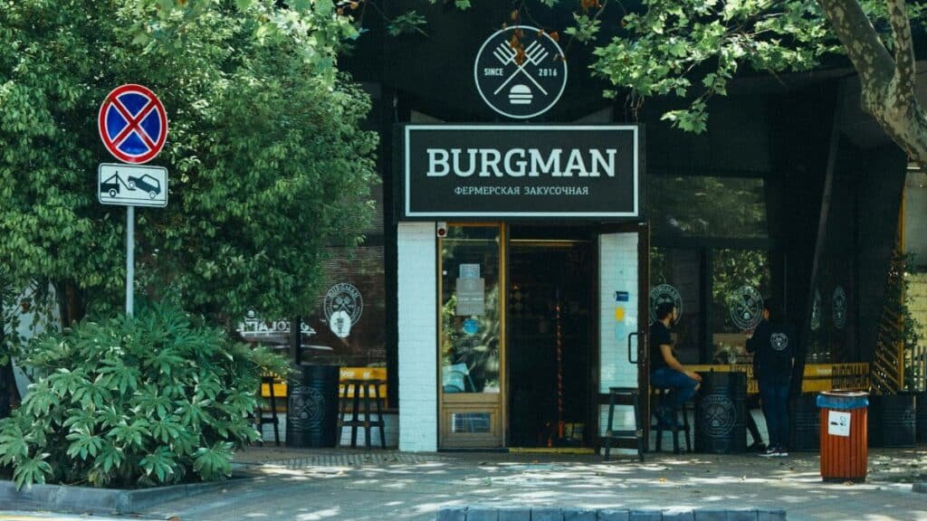 Exterior view of Burgman restaurant with outdoor seating area in a leafy urban setting.