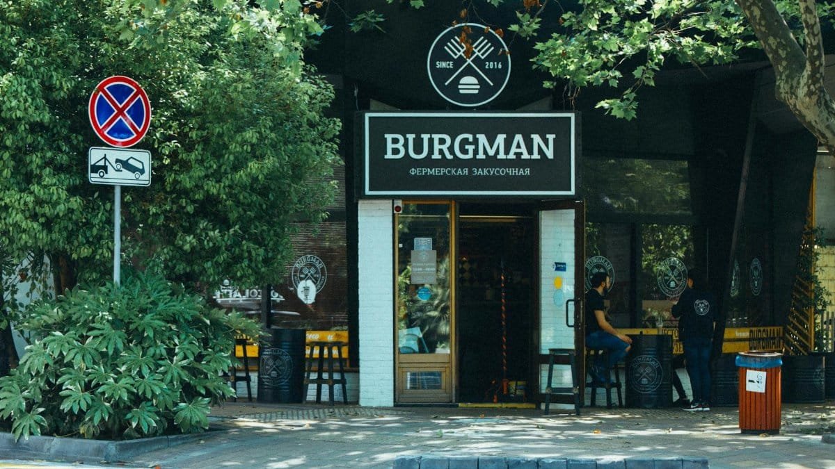 Exterior view of Burgman restaurant with outdoor seating area in a leafy urban setting.