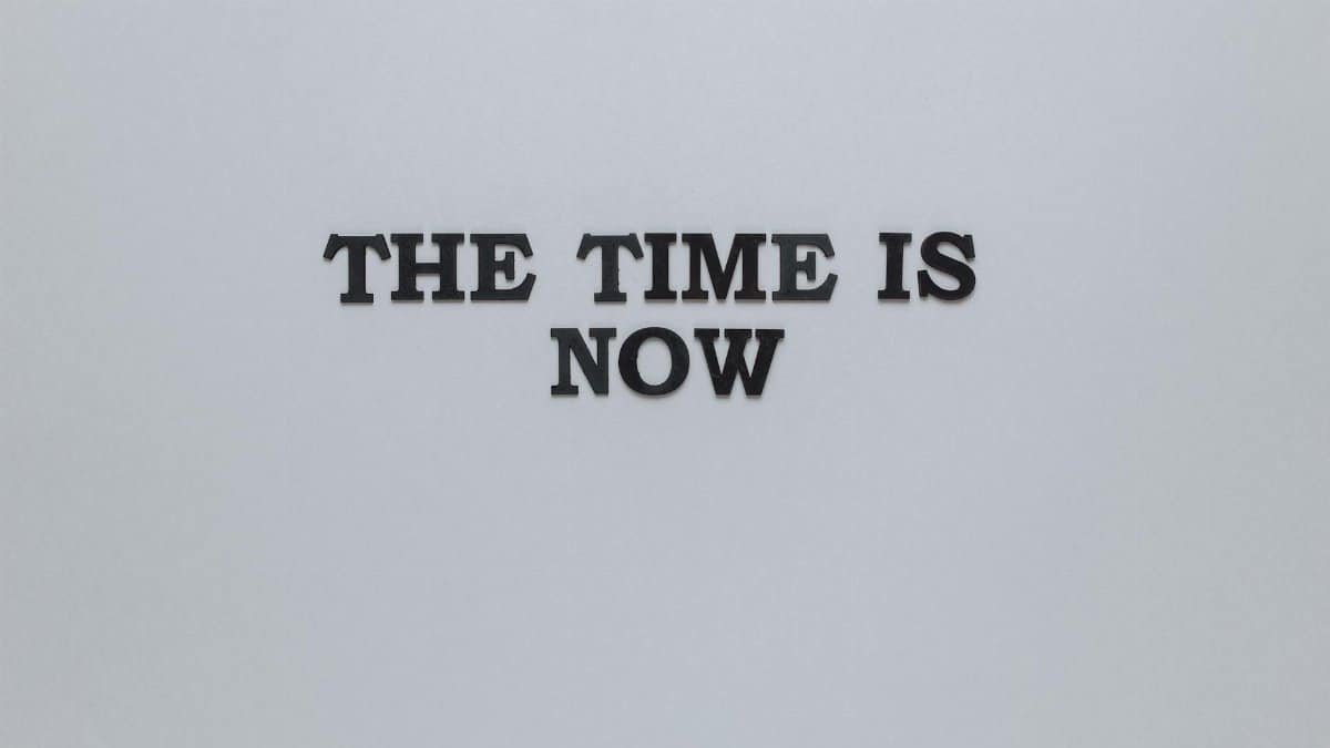 Minimalist poster with the motivational quote 'The Time is Now' on a gray background.