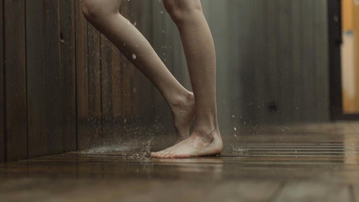 Close-up of a person standing barefoot on a wet wooden floor indoors.