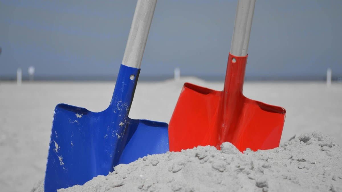 Close-up of colorful shovels in sand at a beach, perfect for summer themes.