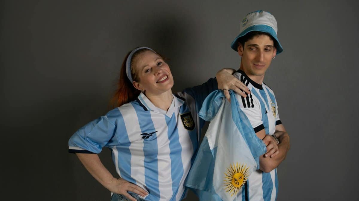 Two joyful Argentina soccer fans in team jerseys with a national flag, celebrating enthusiastically.