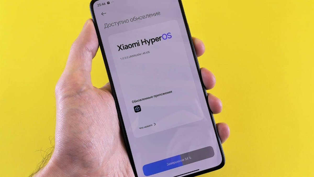 Close-up of a hand holding a smartphone displaying Xiaomi HyperOS update screen on a yellow background.