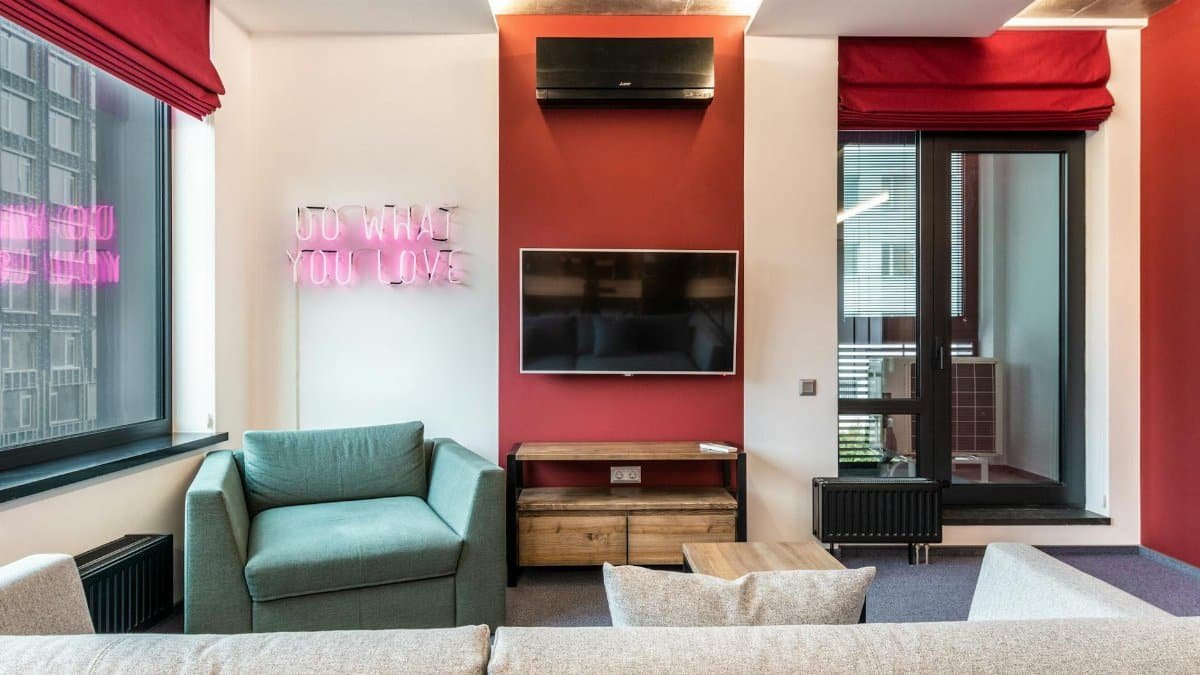 Interior of modern office lounge zone with sofa and armchair with table near window next to TV on wall and neon signboard with text do what you love near door