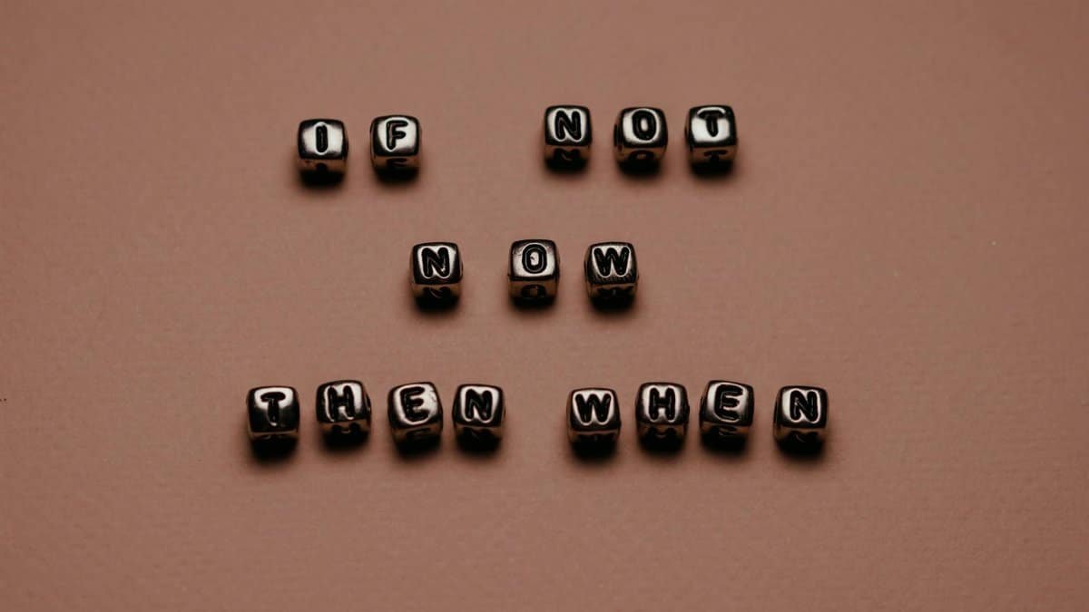 Metal letter cubes spelling 'If not now, then when' on a beige surface, promoting motivation.