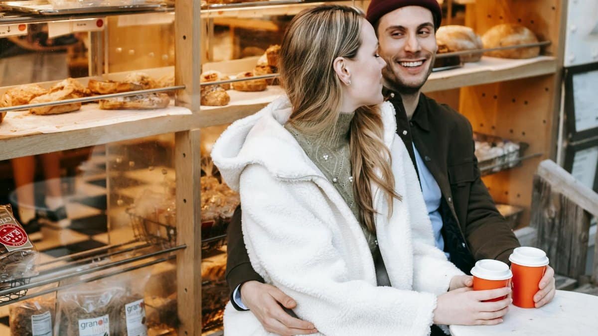 Happy couple enjoying a cozy coffee date outside a bakery with warm drinks.