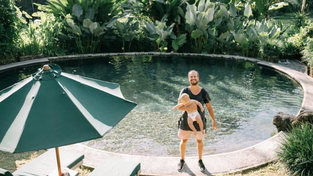 Father holding child by a serene tropical pool, enjoying a sunny day.
