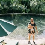 Father holding child by a serene tropical pool, enjoying a sunny day.