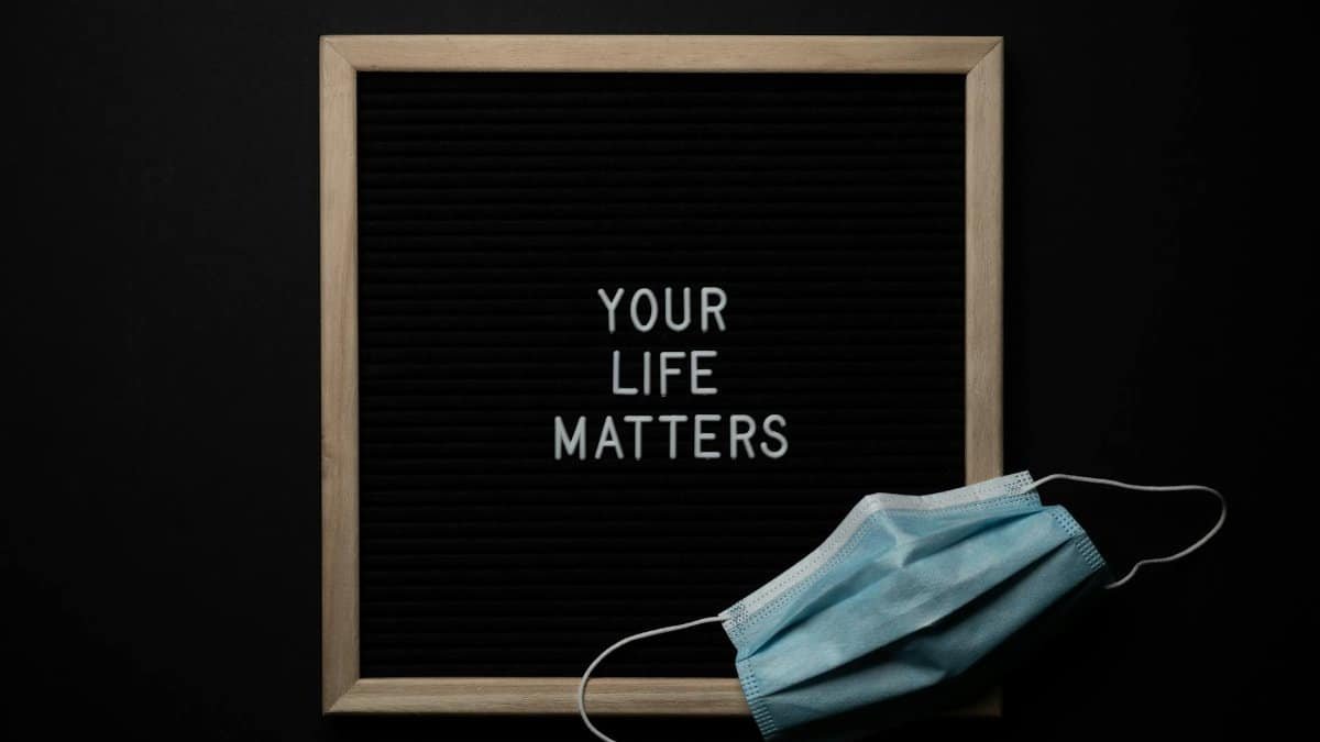 Overhead arrangement of framed black photo with white words Your Life Matters on black background near medical mask