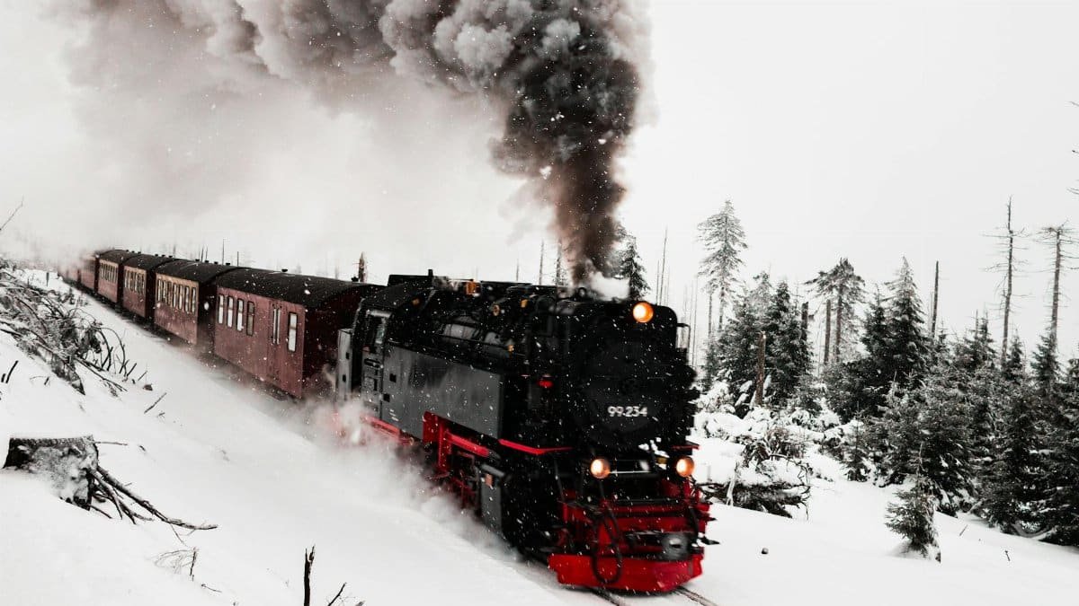 A classic steam train travels through a snowy forest, emitting thick smoke on a winter day.