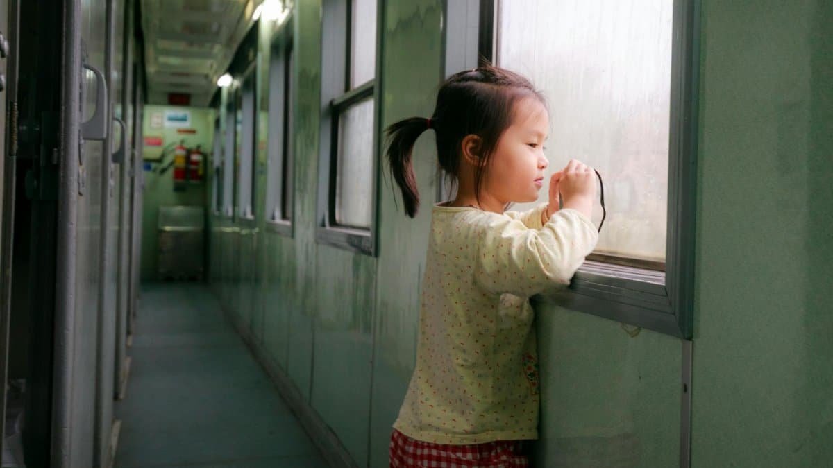 A young girl stands by a train window, looking out thoughtfully while traveling.