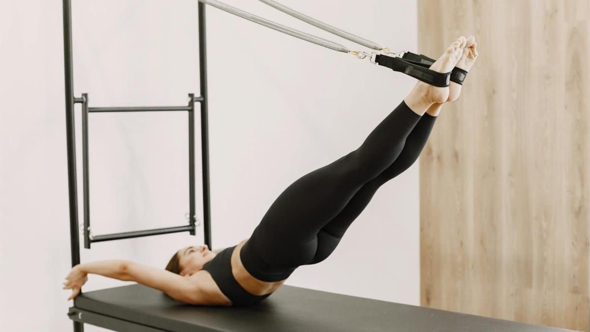 Woman practicing Pilates on a reformer, demonstrating core strength and flexibility in an indoor gym setting.
