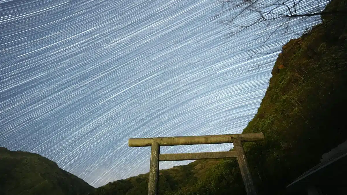 Captivating star trails arc over a traditional Torii gate in a serene night landscape.