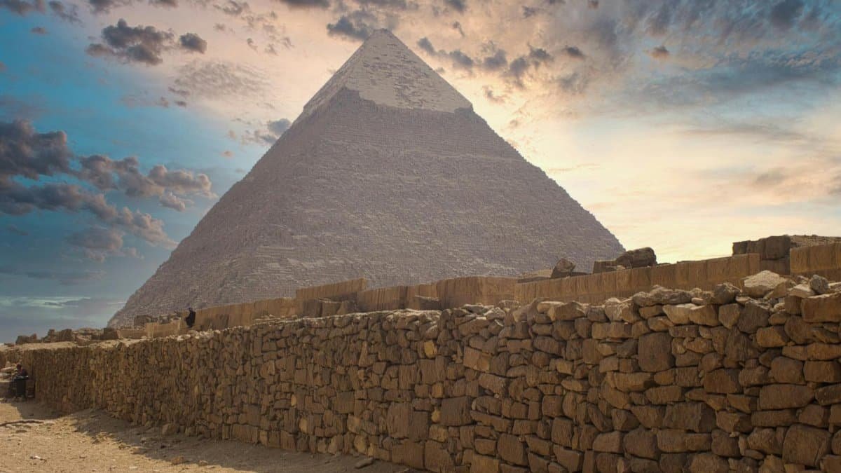 Majestic view of the Great Pyramid of Giza under a dramatic sunset sky in Cairo, Egypt.