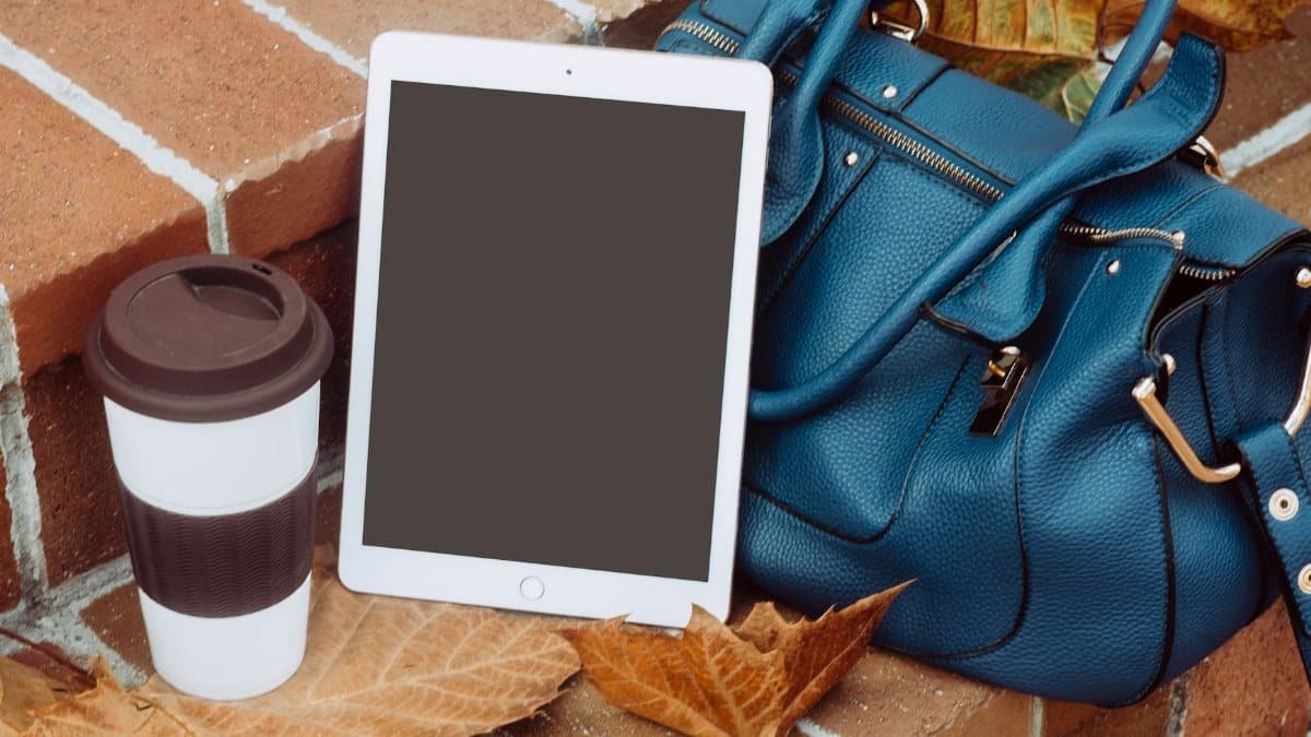 A stylish autumn still life with a coffee cup, tablet, and blue leather bag on brick steps adorned with fall leaves.