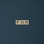 Artistic display of Scrabble tiles spelling the word 'For' on a dark background.