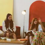 A group of four women casually discussing books in a cozy, colorful room.