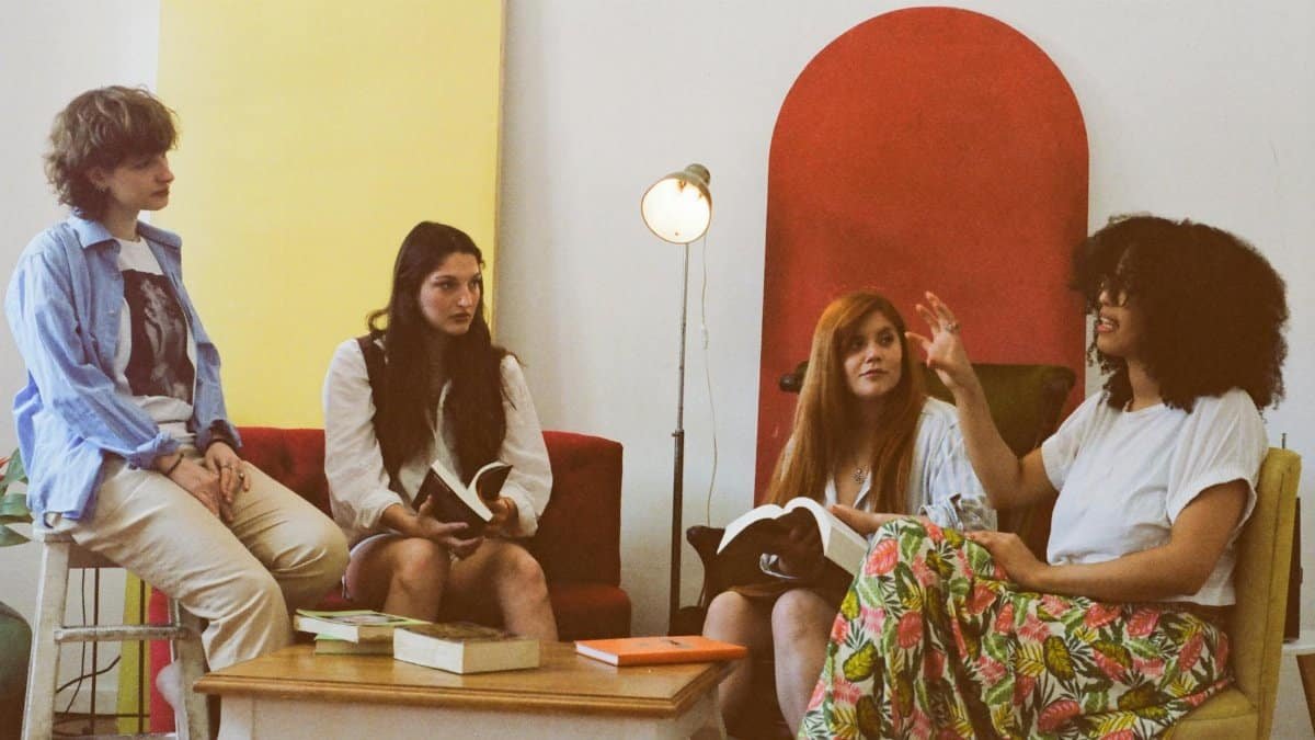 A group of four women casually discussing books in a cozy, colorful room.