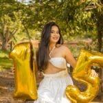 A joyful young woman in white dress celebrating her 15th birthday with balloons outdoors.