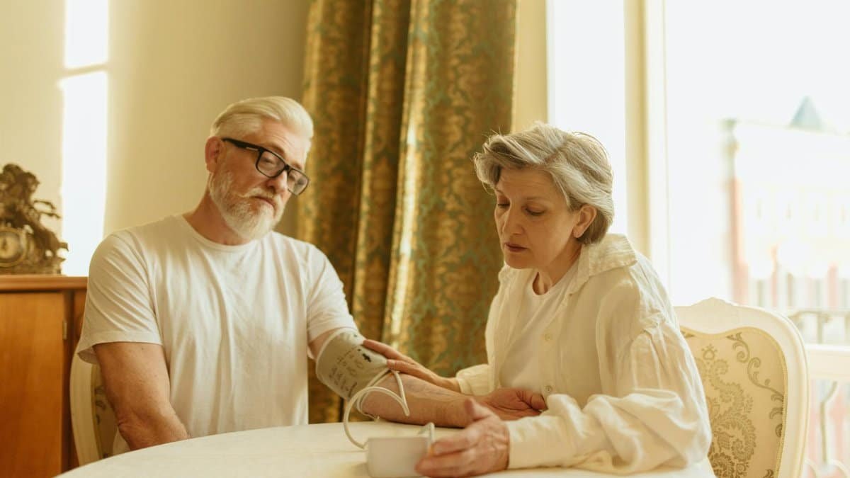 An elderly couple at home measuring blood pressure with a digital monitor, depicting care and health awareness.