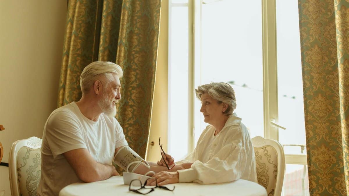 Senior couple using blood pressure monitor at home, fostering health awareness and companionship.