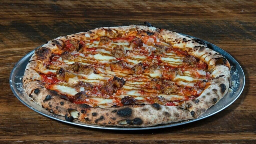 Delicious wood-fired pizza with Italian sausage on a metal tray. Perfect for food lovers.