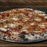 Delicious wood-fired pizza with Italian sausage on a metal tray. Perfect for food lovers.