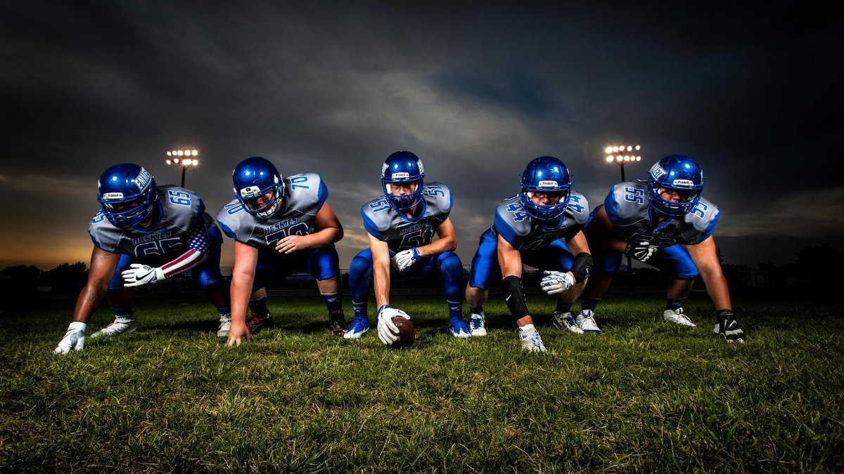 A cohesive football team lines up on the field under stadium lights, prepared for the game ahead.