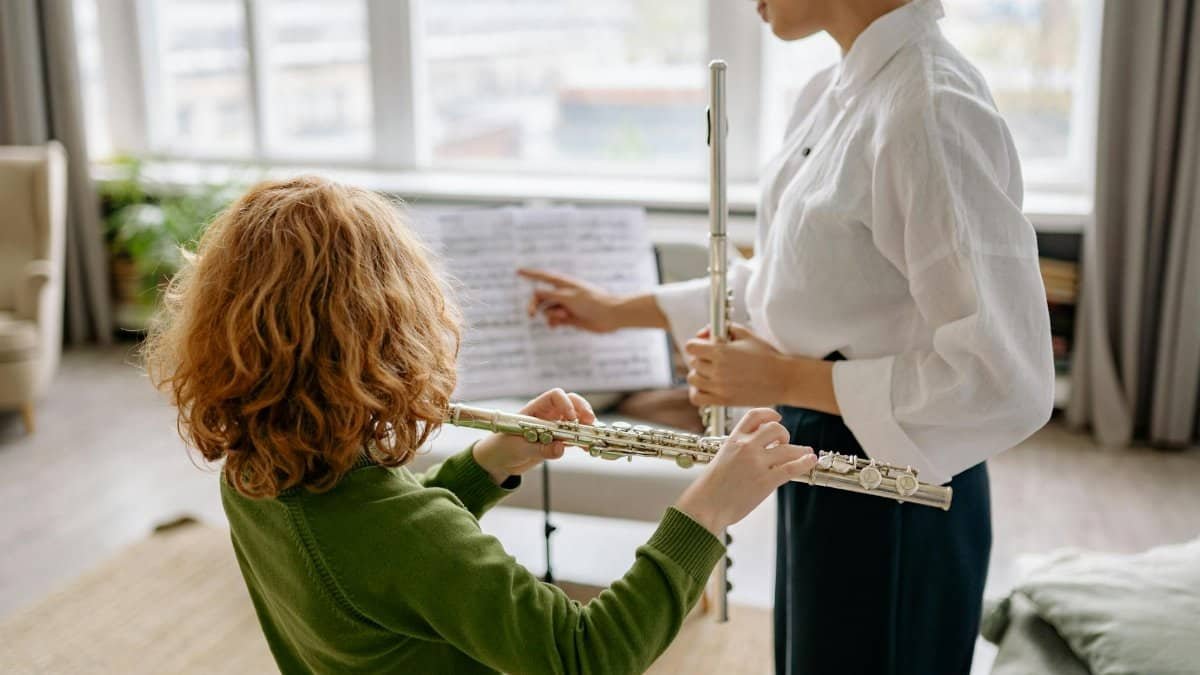 A child receiving a flute lesson from a teacher at home, both holding woodwind instruments.