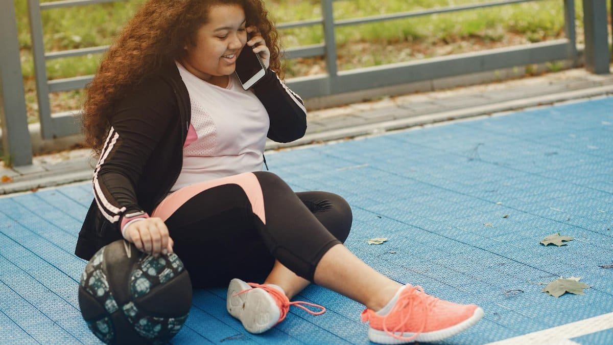 Smiling woman multitasks exercise and phone call on outdoor track.