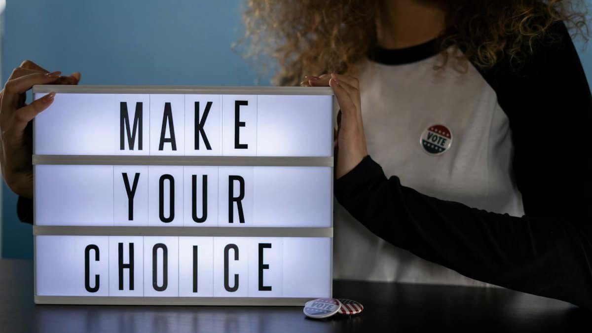 Woman holding lightbox with 'Make Your Choice' promoting civic duty and voting.