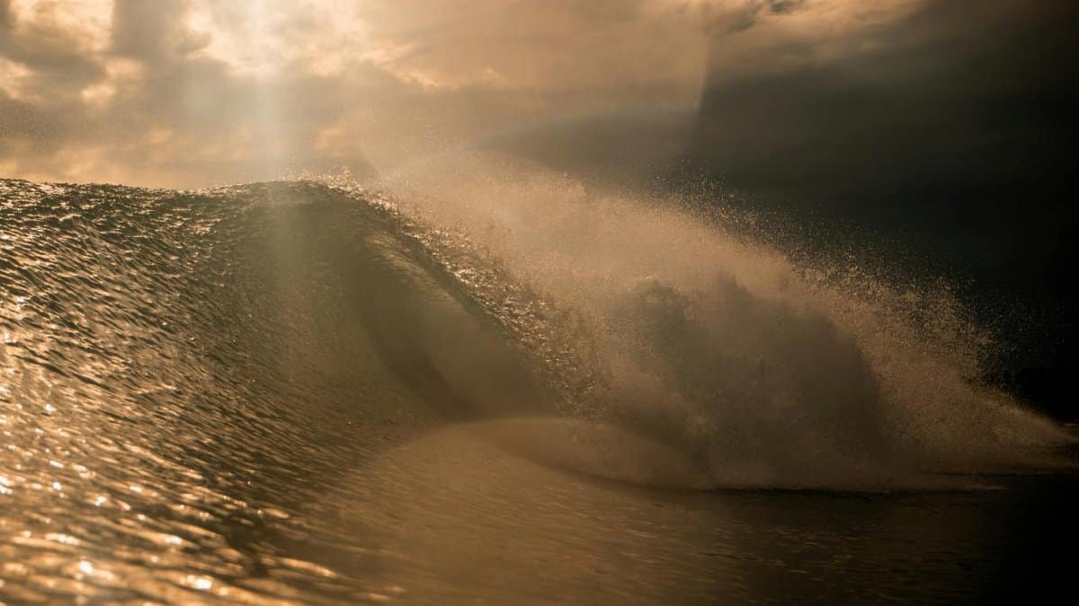 A stunning sunset wave captures the dramatic ocean scene, enhanced by striking sunbeams.
