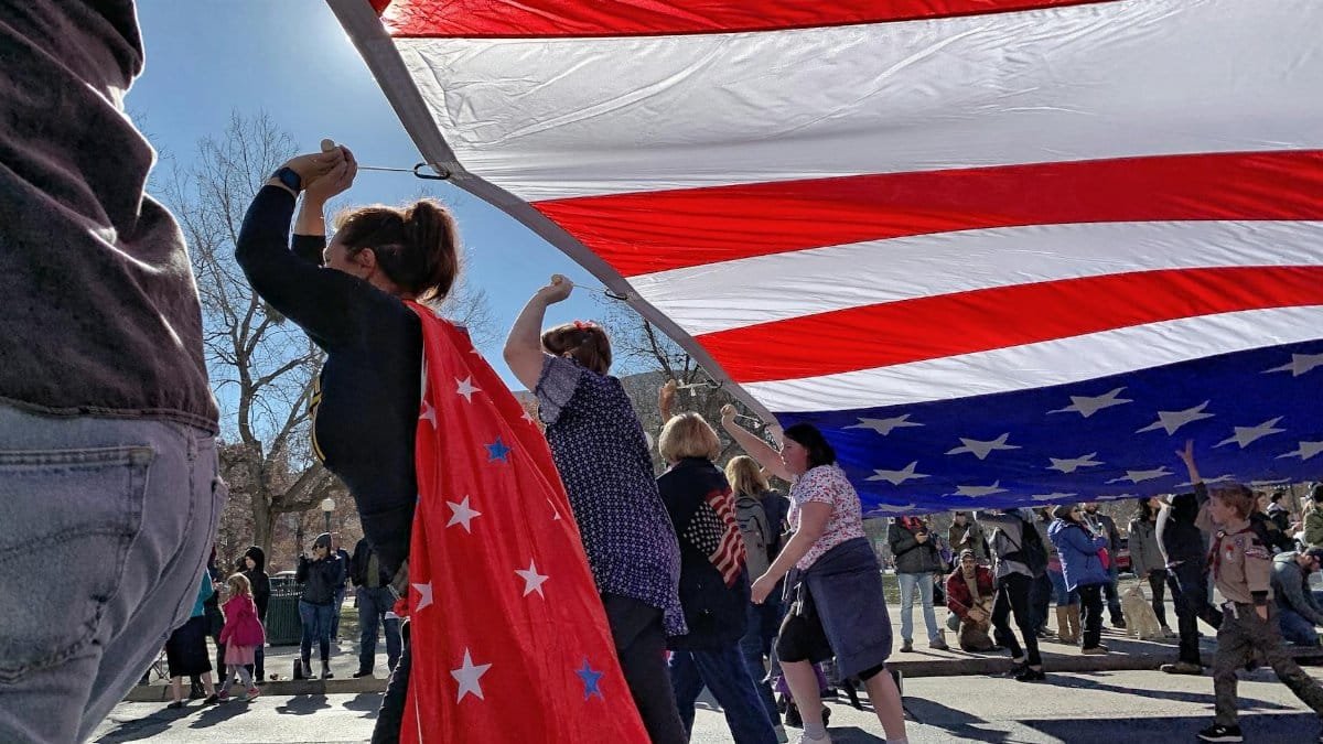 People celebrating under a massive American flag at a parade in Denver, CO, showcasing patriotism and community spirit.