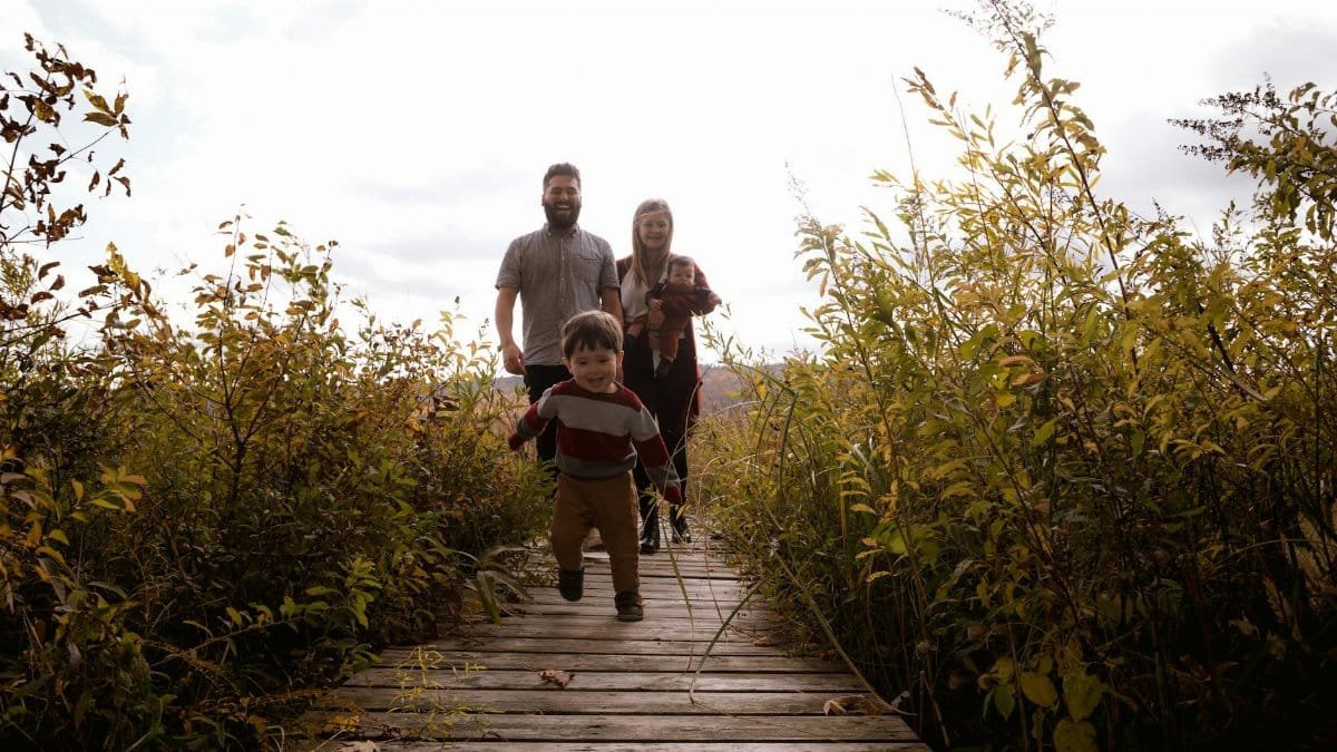 A joyful family walking on a wooden path surrounded by lush greenery in the fall.