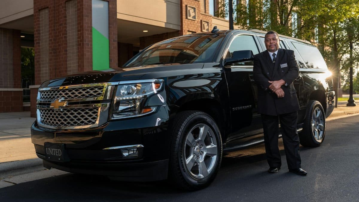 Chauffeur standing confidently next to a black SUV, offering luxury transportation service.