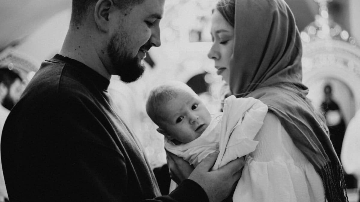 Heartwarming black and white photo of a family with their baby during a christening ceremony.