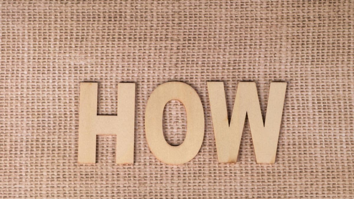 Word 'HOW' formed with wooden letters on textured burlap surface.