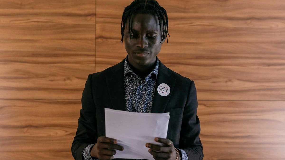 Black man wearing a suit addressing a document, possibly in a political setting.
