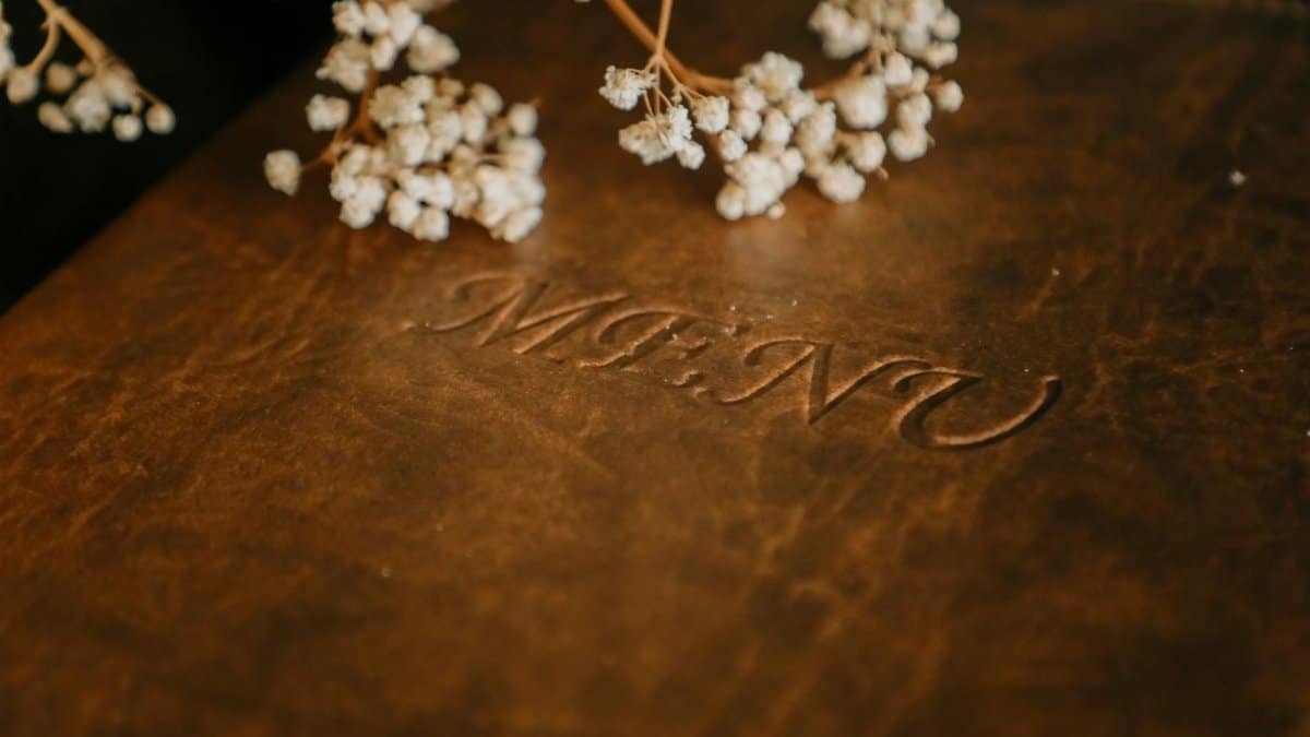 Close-up of a brown leather menu adorned with baby's breath flowers, perfect for upscale restaurant settings.