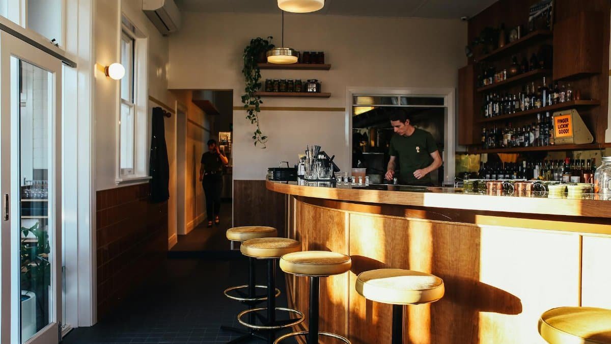 A warm and inviting indoor bar with stools and a bartender preparing drinks.
