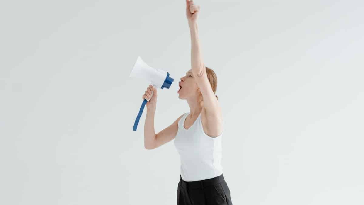 A confident woman raises her arm while shouting into a megaphone, symbolizing leadership and empowerment.